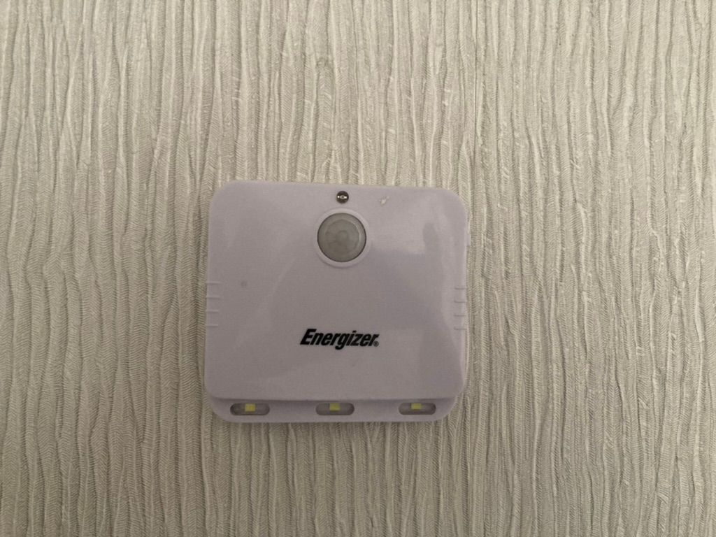 A small white LED motion sensor light mounted on a textured wall.