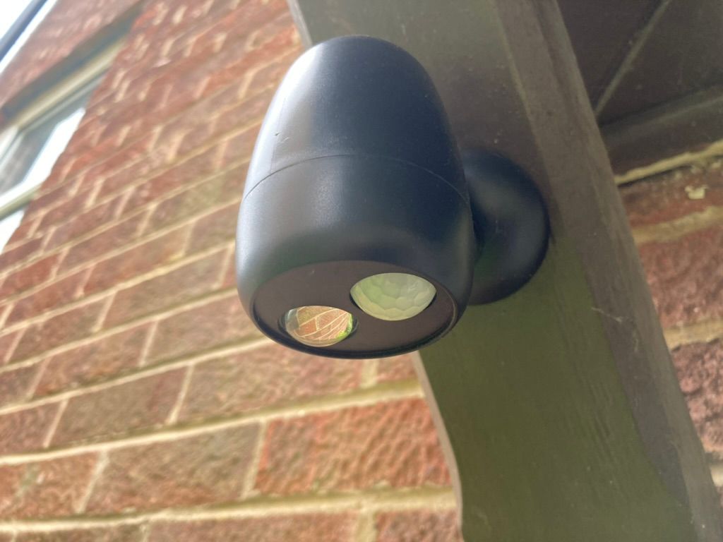 A black LED security light mounted on a brick wall outdoors.