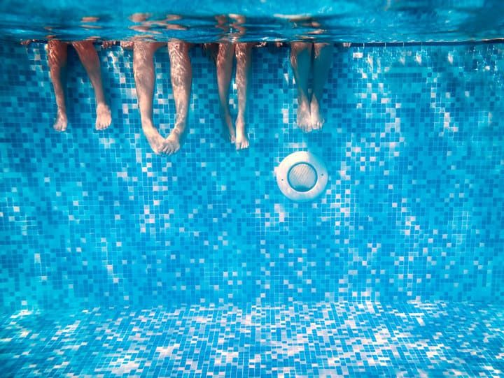 Four pairs of feet submerged in a blue tiled swimming pool.