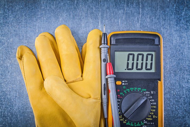 Yellow gloves next to a multimeter displaying a zero reading on a textured background.
