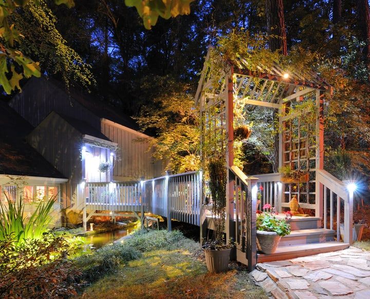 A well-lit garden pathway and pergola at twilight with plants.