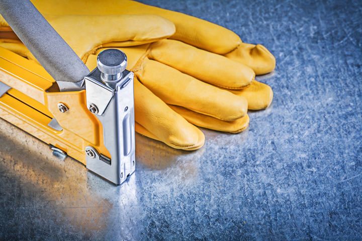 A metal stapler beside a pair of yellow work gloves on a textured surface.