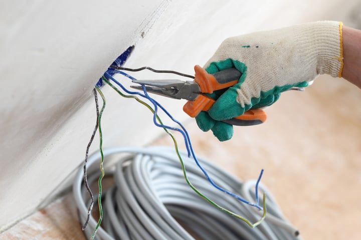 Person using pliers to cut electrical wires from a wall.