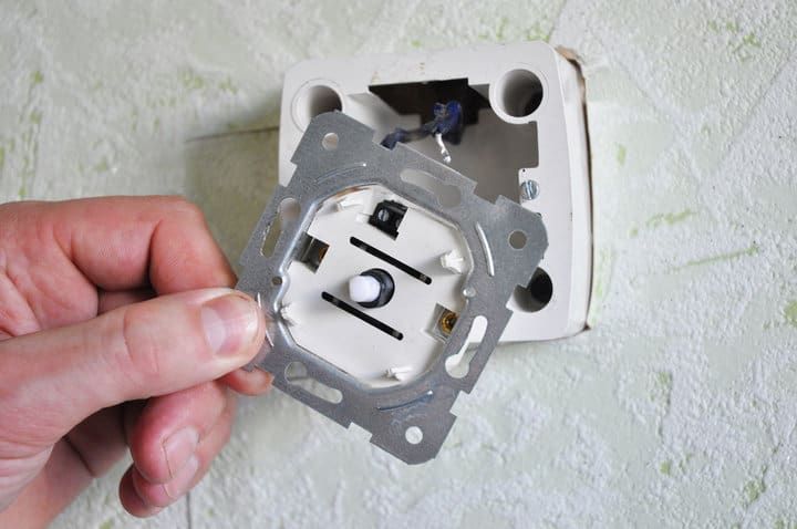 Hand holding a metal mounting plate for an LED light fixture installation.