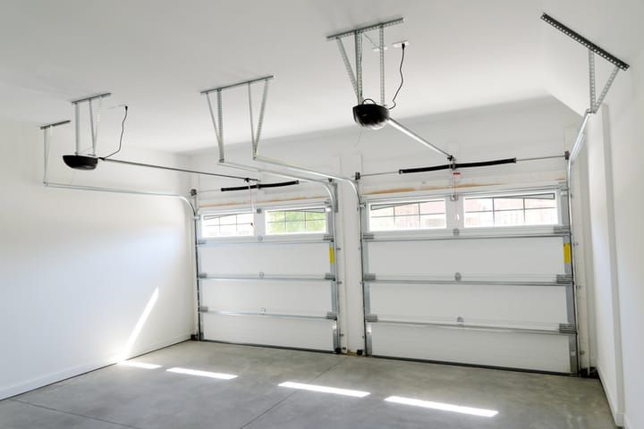 Brightly lit garage with two garage doors and overhead tracks.