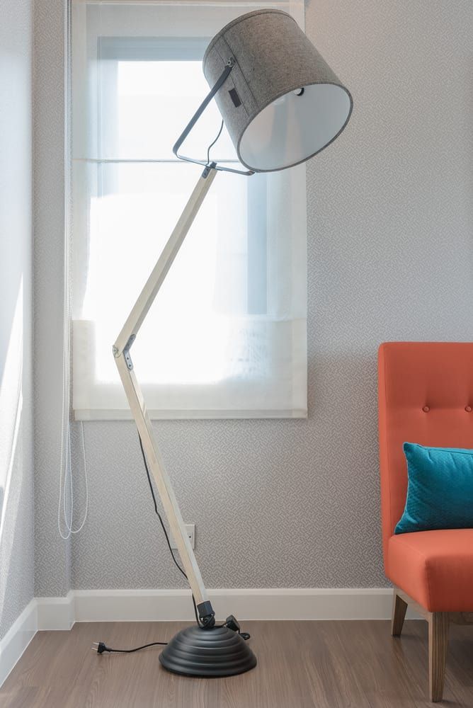 A stylish floor lamp with a gray shade and wooden stand beside an orange chair.