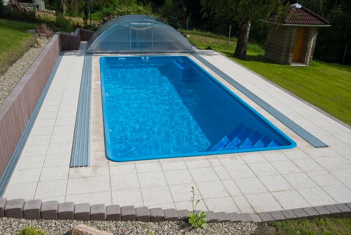 A clear swimming pool surrounded by a paved area and grass.