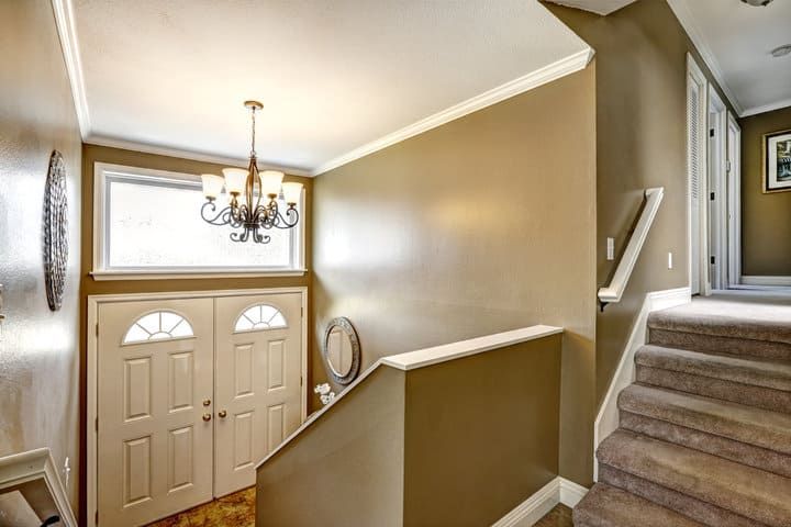 Brightly lit hallway with a chandelier, stairs, and mirrored decor.