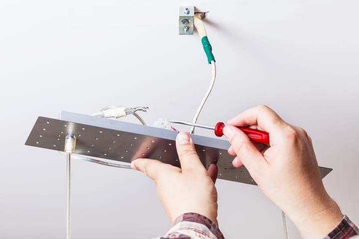 Person installing an LED light fixture on a ceiling, using tools.