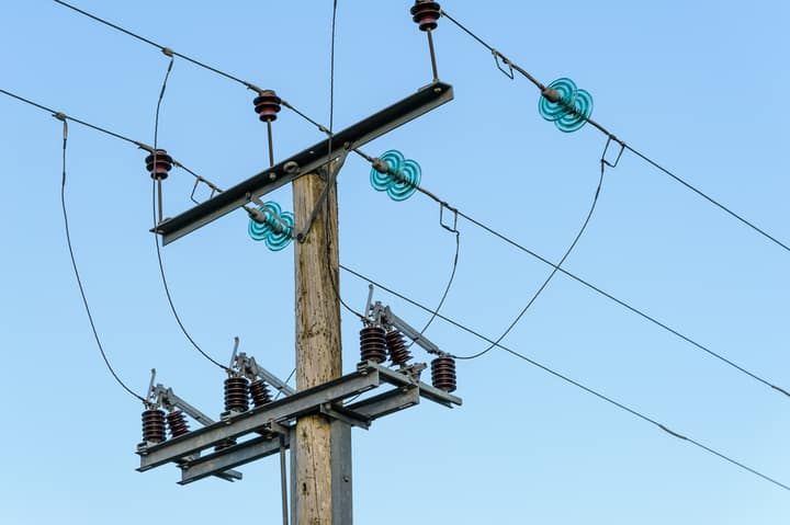 Utility pole with electrical lines and insulators against a clear blue sky.