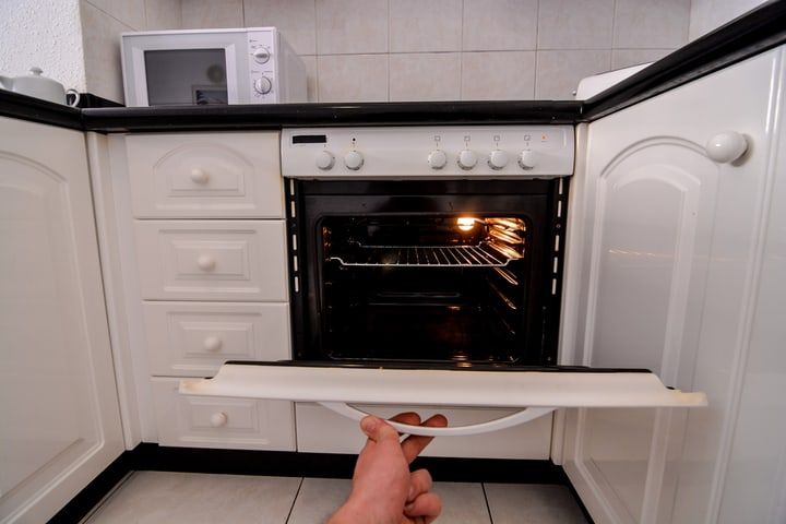 A hand pulls open the oven door in a modern kitchen.