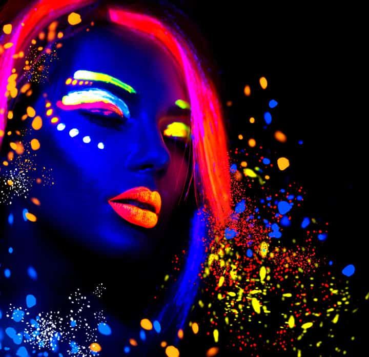 A woman with vibrant neon face paint glows against a dark background.
