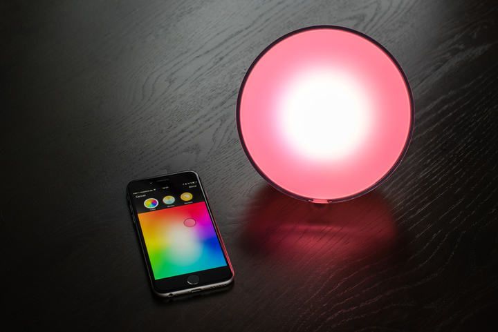 A round LED lamp glowing pink next to a smartphone with a color selection app.