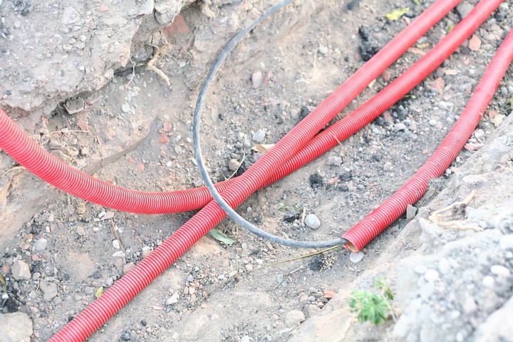 Red electrical conduit hoses laid in a trench among dirt and rocks.