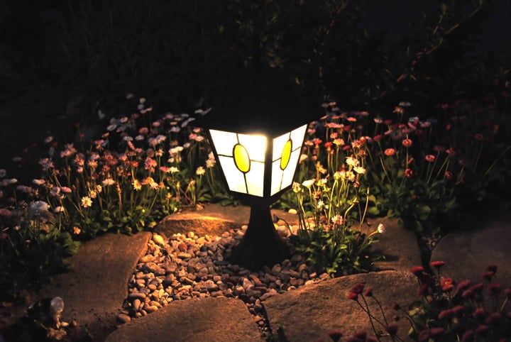 A decorative garden lantern illuminates colorful flowers at night.