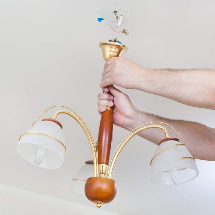 A person is installing a chandelier with multiple glass shades on the ceiling.