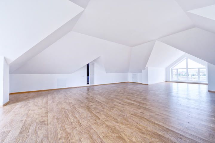 Spacious, modern attic room with wooden flooring and slanted white walls.