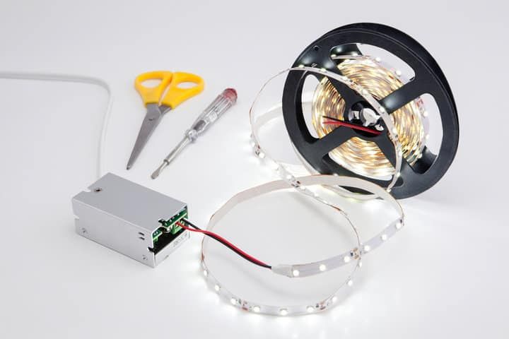 A roll of LED light strip, a power supply, and scissors on a white surface.