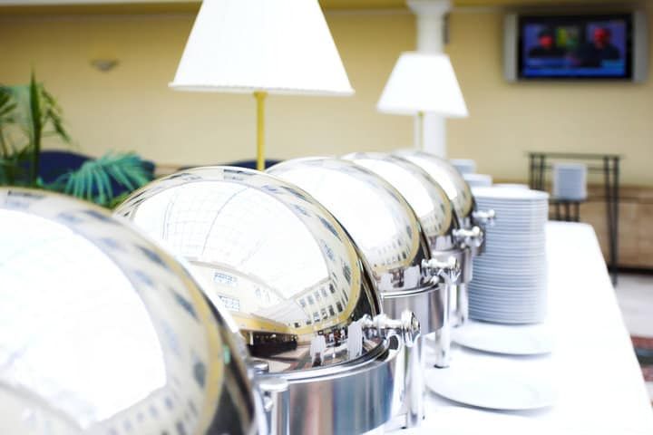 Line of shiny food warmers on a banquet table with plates.