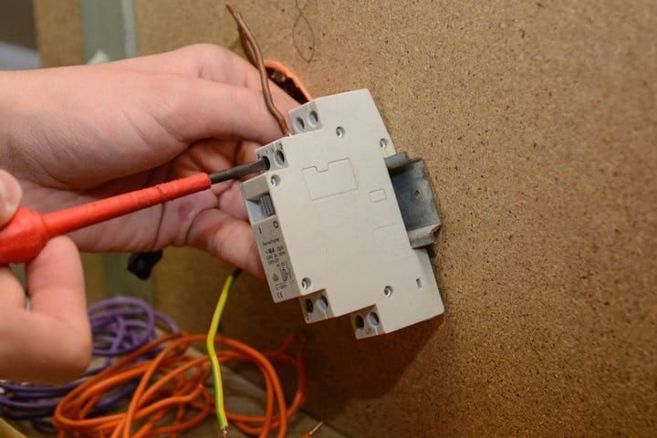 Hand holding a screwdriver, adjusting a circuit breaker mounted on a wall.