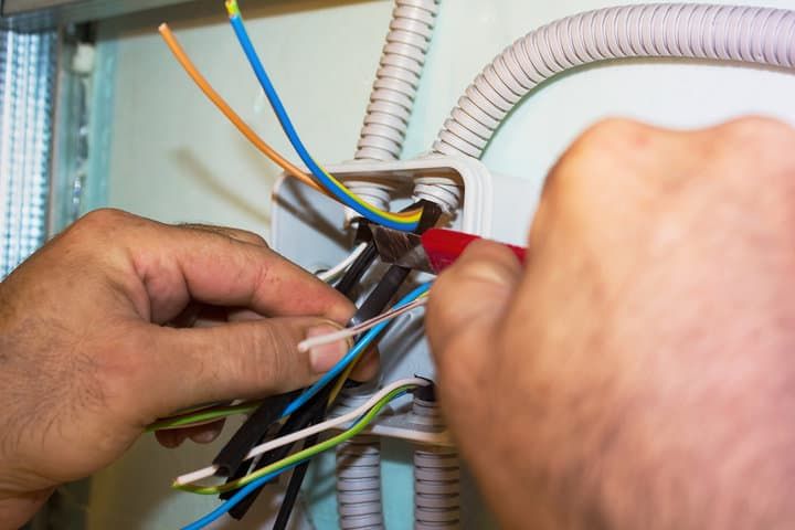 Hands working with colorful wires inside an electrical junction box.