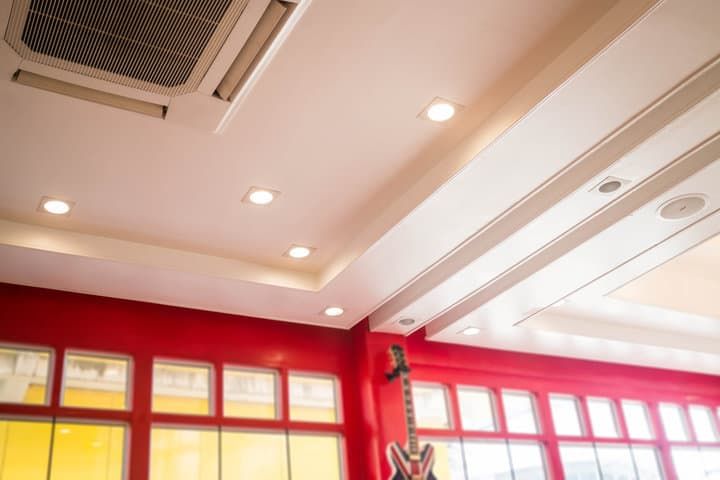 Bright recessed LED lights illuminate a room with red walls and large windows.