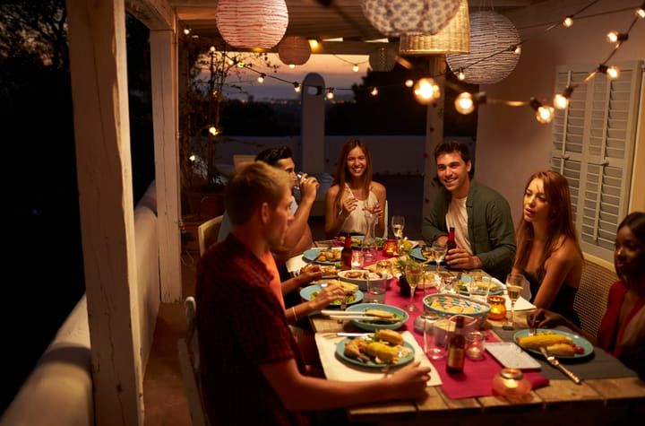 Group of friends enjoying dinner together under string lights and lanterns.