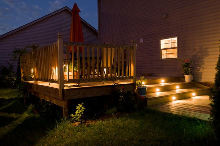 A beautifully lit wooden deck at night with an umbrella and plants.
