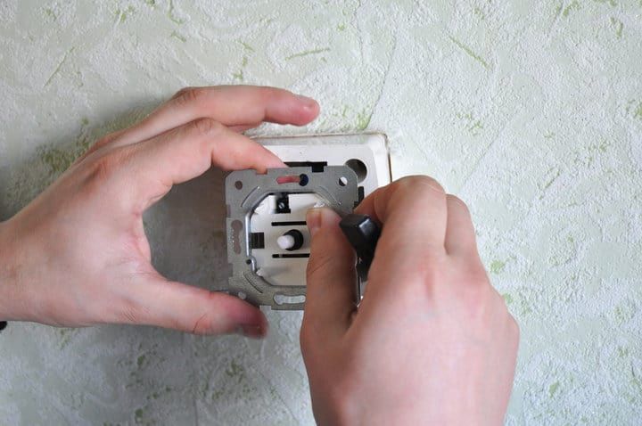 A person installing a light fixture base on a wall.