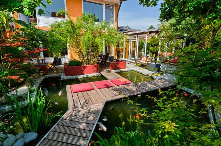 A serene garden with a pond, wooden bridge, and colorful plants.