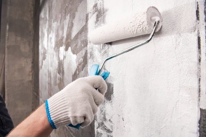 A person painting a wall with a roller in gray tones.