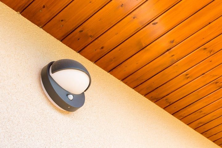 A modern LED wall light mounted on a textured wall beneath wooden beams.