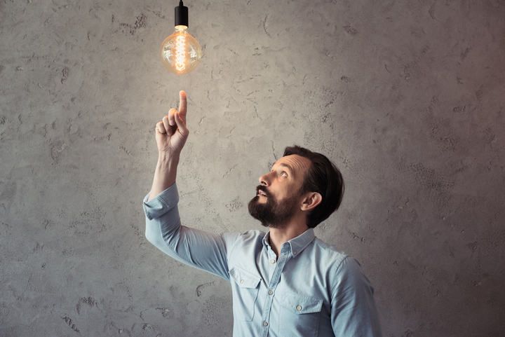 A man points at a glowing LED light bulb hanging from the ceiling.