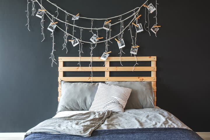 Wooden bed frame with pillows and string lights holding photos.