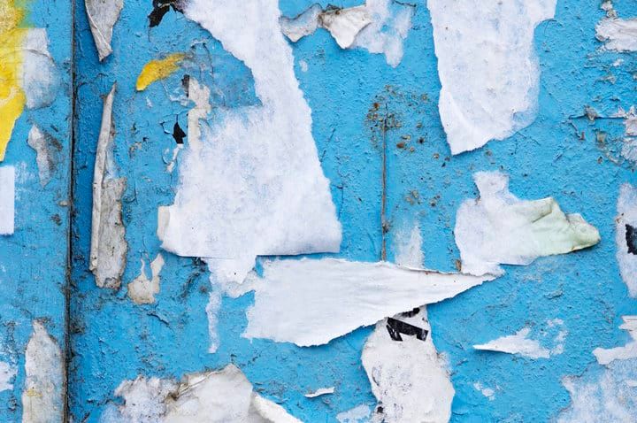 Close-up of a textured wall with peeling blue paint and white paper scraps.