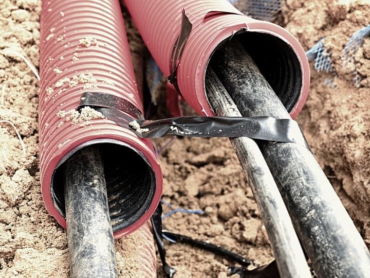 Close-up of black cables covered by red protective tubing in soil.