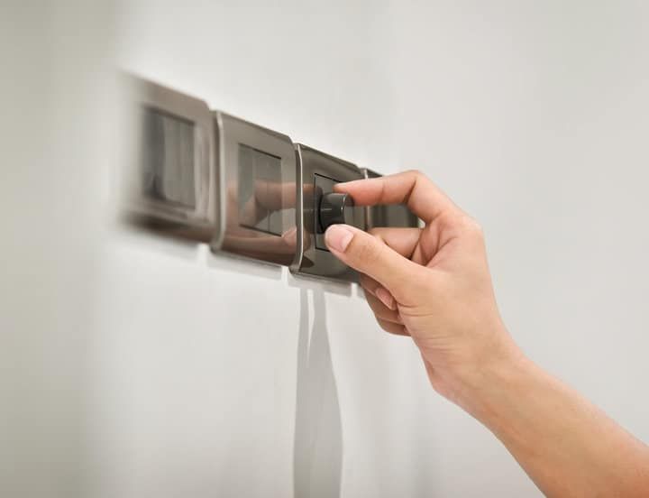 A hand adjusting a dimmer switch on a modern light control panel.
