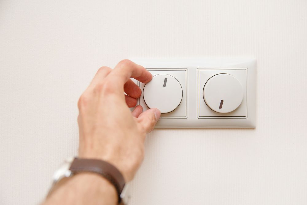 A hand adjusting a round dial on a light switch panel.