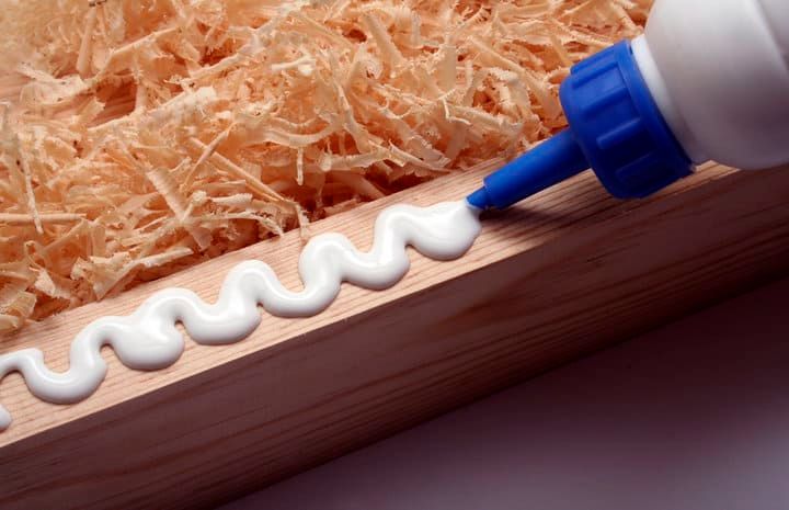 A bottle of white glue dispensing a wavy line onto a wooden surface.