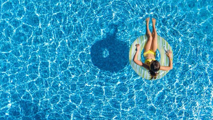 A person relaxes on a float in a clear blue swimming pool.