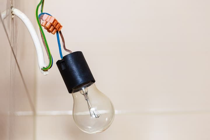 A hanging light bulb fixture with exposed wiring against a neutral background.