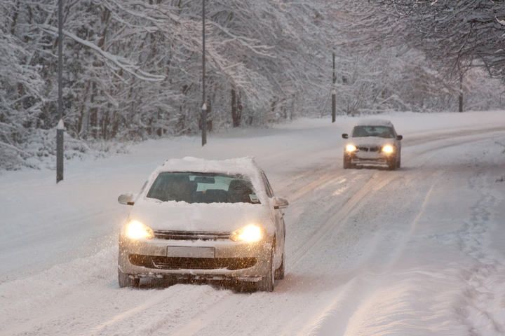 Two cars navigating a snowy road lined with trees.
