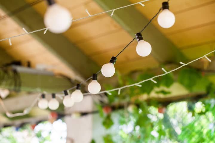 String lights with white bulbs hang under a wooden structure and greenery.