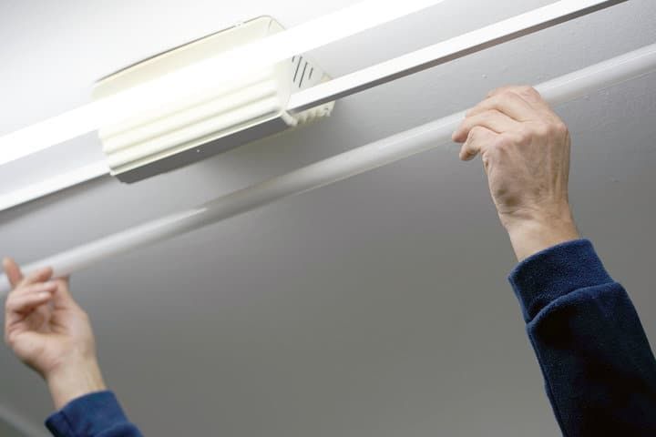 Two hands installing an LED light tube into a ceiling fixture.