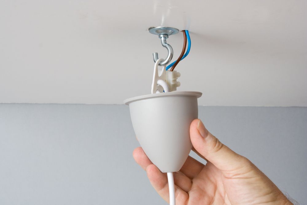 Hand holding a light fixture with electrical wires attached to the ceiling.