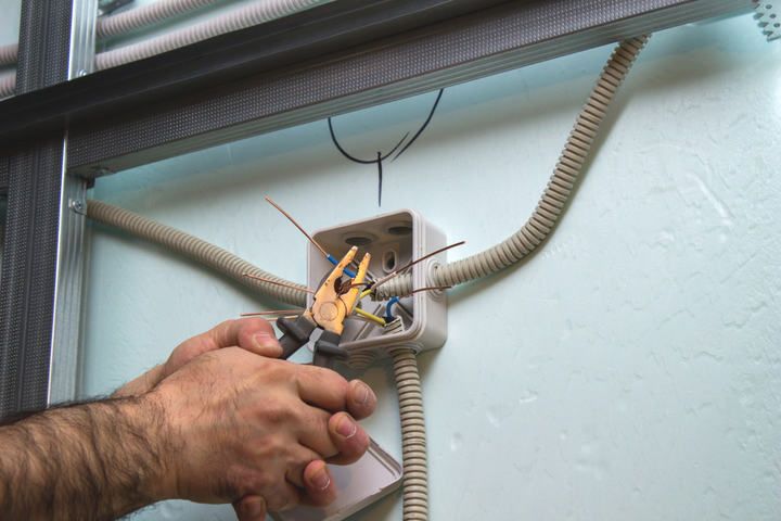 Hands working on wiring inside an electrical junction box with tools.