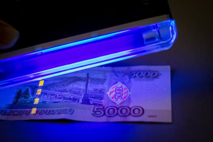 A blue LED light illuminates a 5000 ruble banknote revealing security features.