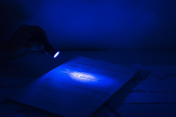 A hand holding a flashlight illuminating text on paper in blue light.