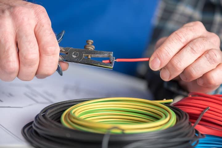 Person using wire strippers on a red electrical wire, surrounded by colorful cables.