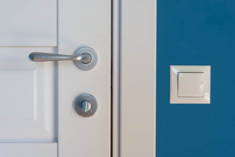 Close-up of a door handle next to a light switch on a blue wall.